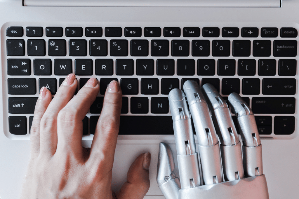 Mano humana y mano robótica escribiendo juntas en un teclado, simbolizando la colaboración con Jasper AI en tareas de redacción asistida por inteligencia artificial.
