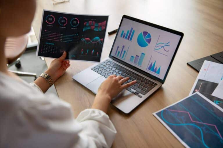 Mujer analizando gráficos en laptop y documentos impresos, ideal para representar la comparación entre data analysis vs data science.